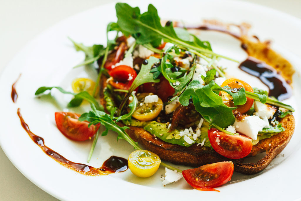 avocado toast with cherry tomatoes, arugula, vegan feta, and a balsamic reduction